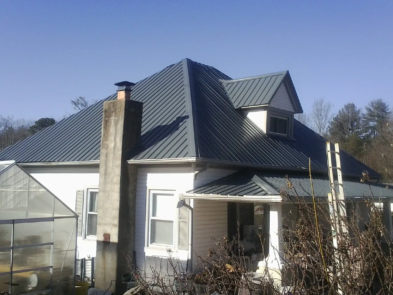 Dark blue standing seam metal roof on a white farmhouse with dormer — Slate & Tile Roof Repair by Roofing Brothers in Alexis