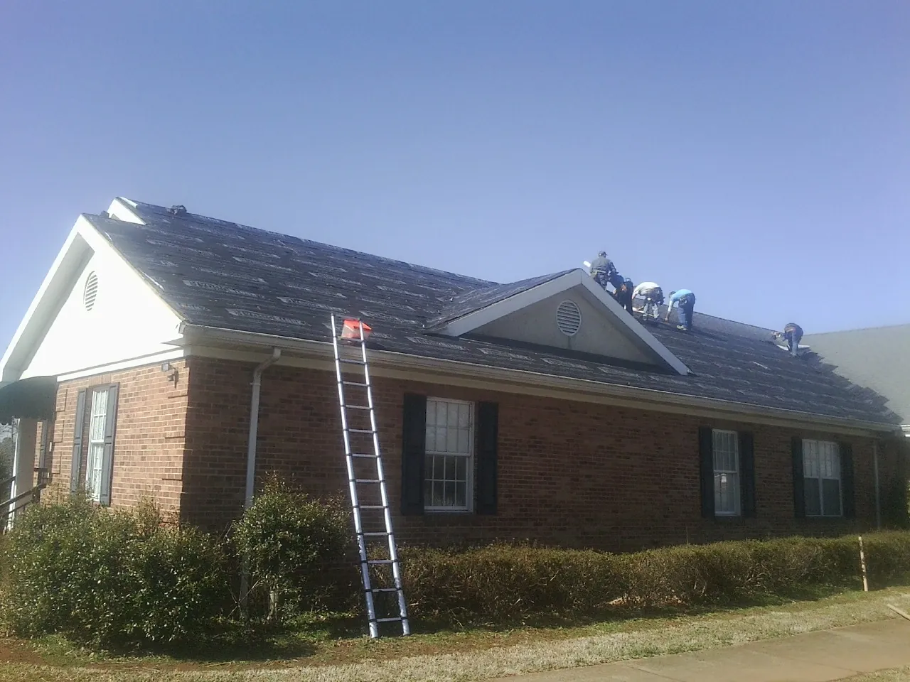 Crew tearing shingles off a brick ranch roof with a ladder set — Emergency Roof Repair work by our crew in Alexis