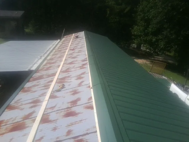 Old rusted panels beside newly installed green metal roofing — Wind Damage Roof Repair by Roofing Brothers in Alexis