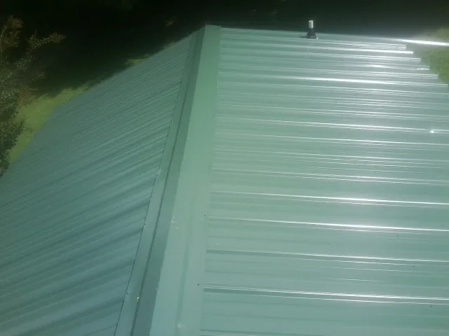 New green metal panels meeting at the ridge of a roof — Flat Roof Repair work by our crew in Alexis