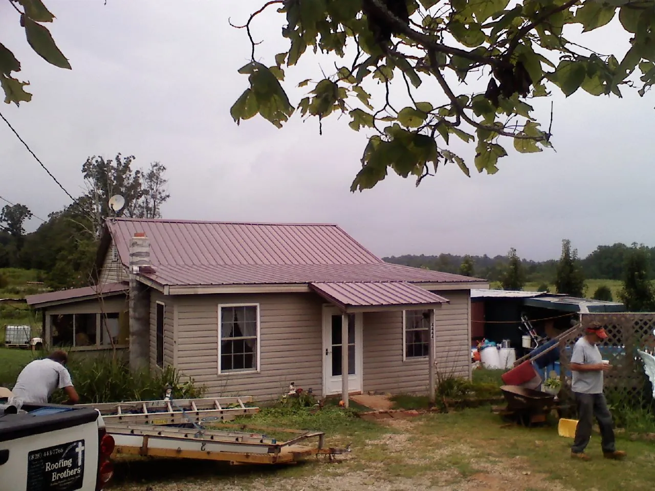Crew finishing a mauve metal roof on a small farmhouse in Alexis