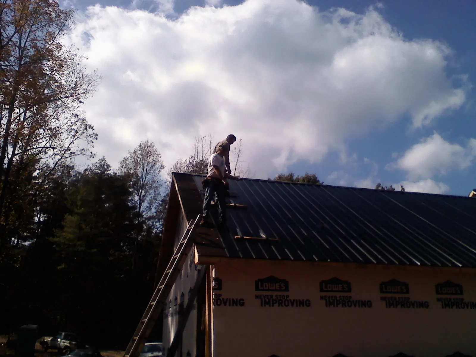 Roofer fastening dark metal panels high against a cloudy sky, from a Roof Inspection job in Alexis