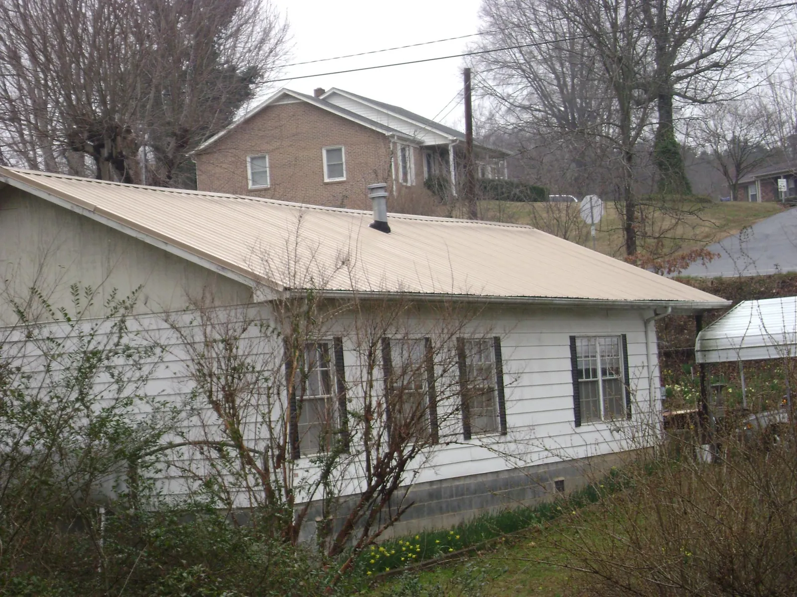 Tan metal roof on a white sided house set into a hillside — Commercial Roofing by Roofing Brothers in Alexis